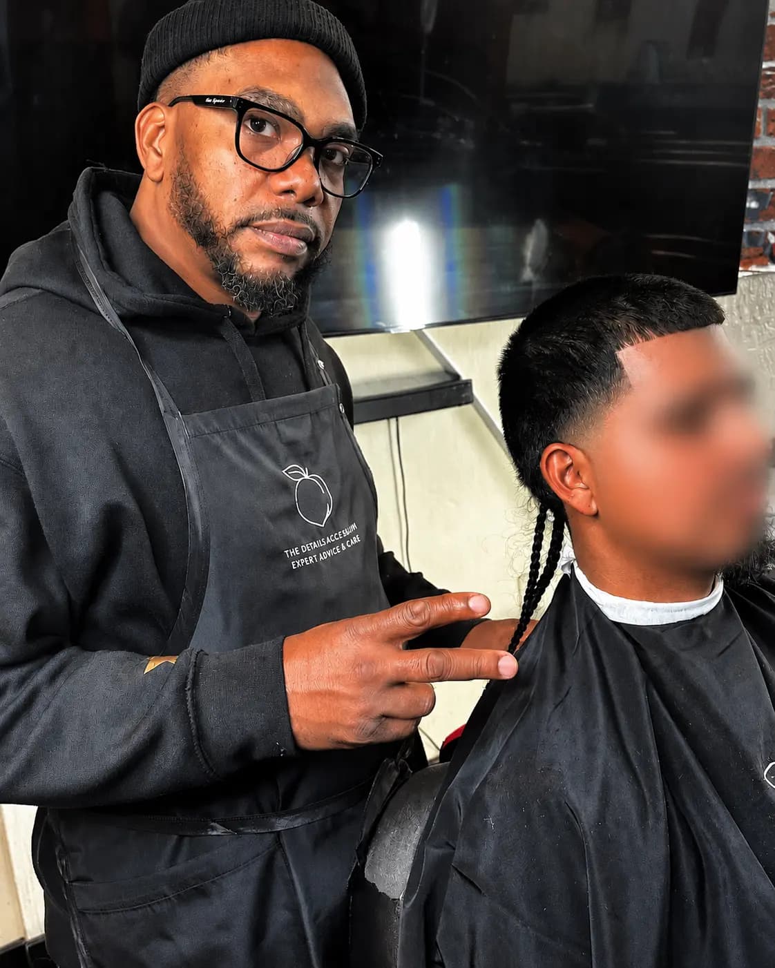 Ali cutting a client's hair at the shop, finishing a taper fade